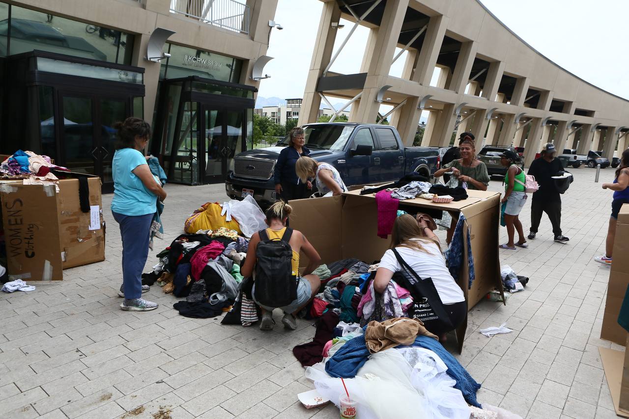 People sort clothing beside large cardboard boxes on a city plaza.